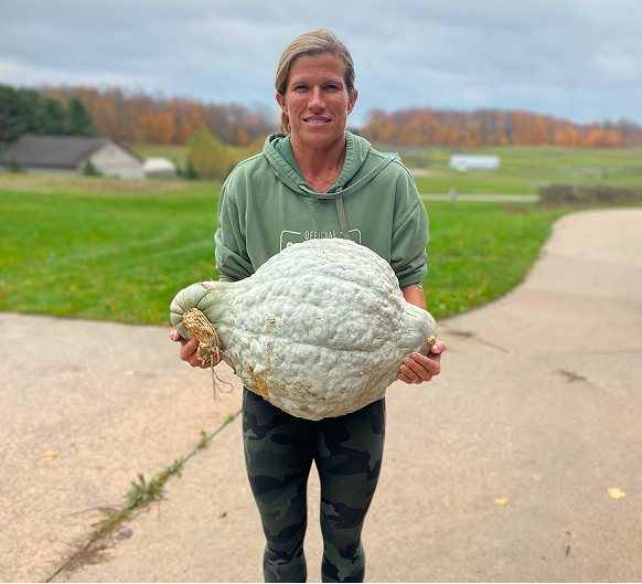 Person holding a large pumpkin outdoors on a road with a scenic background